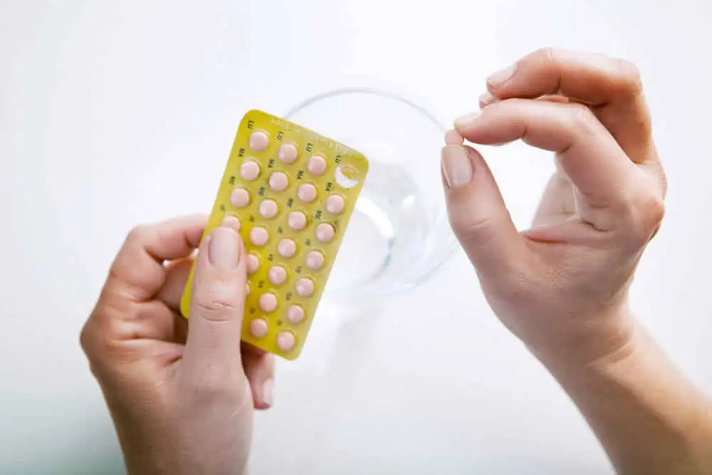Close crop image of hands holding a sleeve of pills, with a glass of water in the background