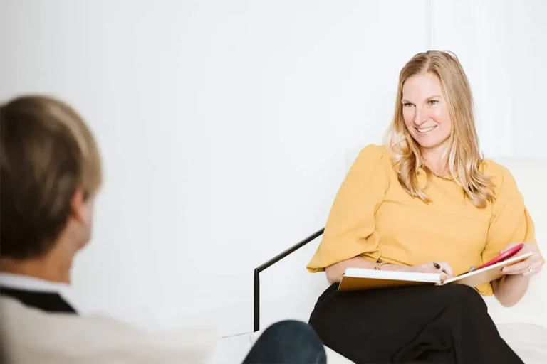 A smiling naturopath actively listening to a patient during a consultation, taking notes to help build a personalized health strategy.
