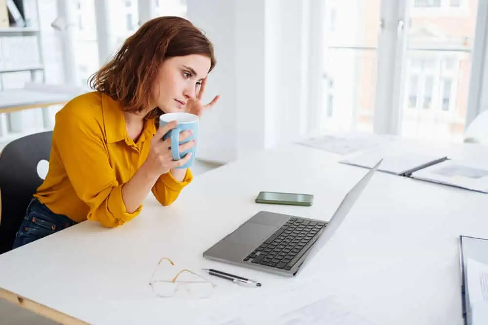 Photo of a woman in a yellow shirt at her desk looking stressed